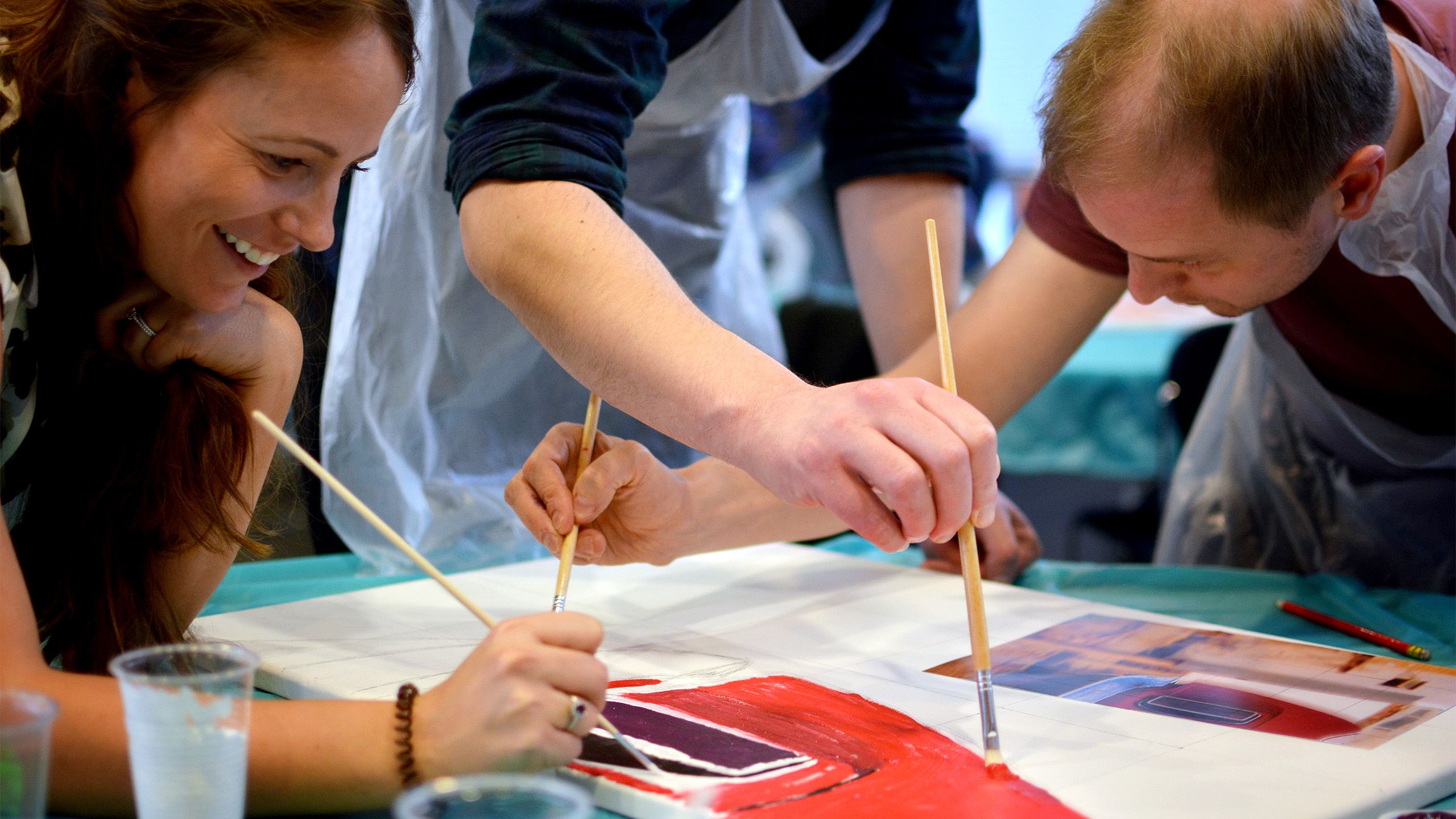 A group of 3 people painting a picture of a car