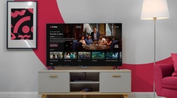 A lounge with a TV on a TV stand with a lamp next to it and the screen displaying the Freely user interface
