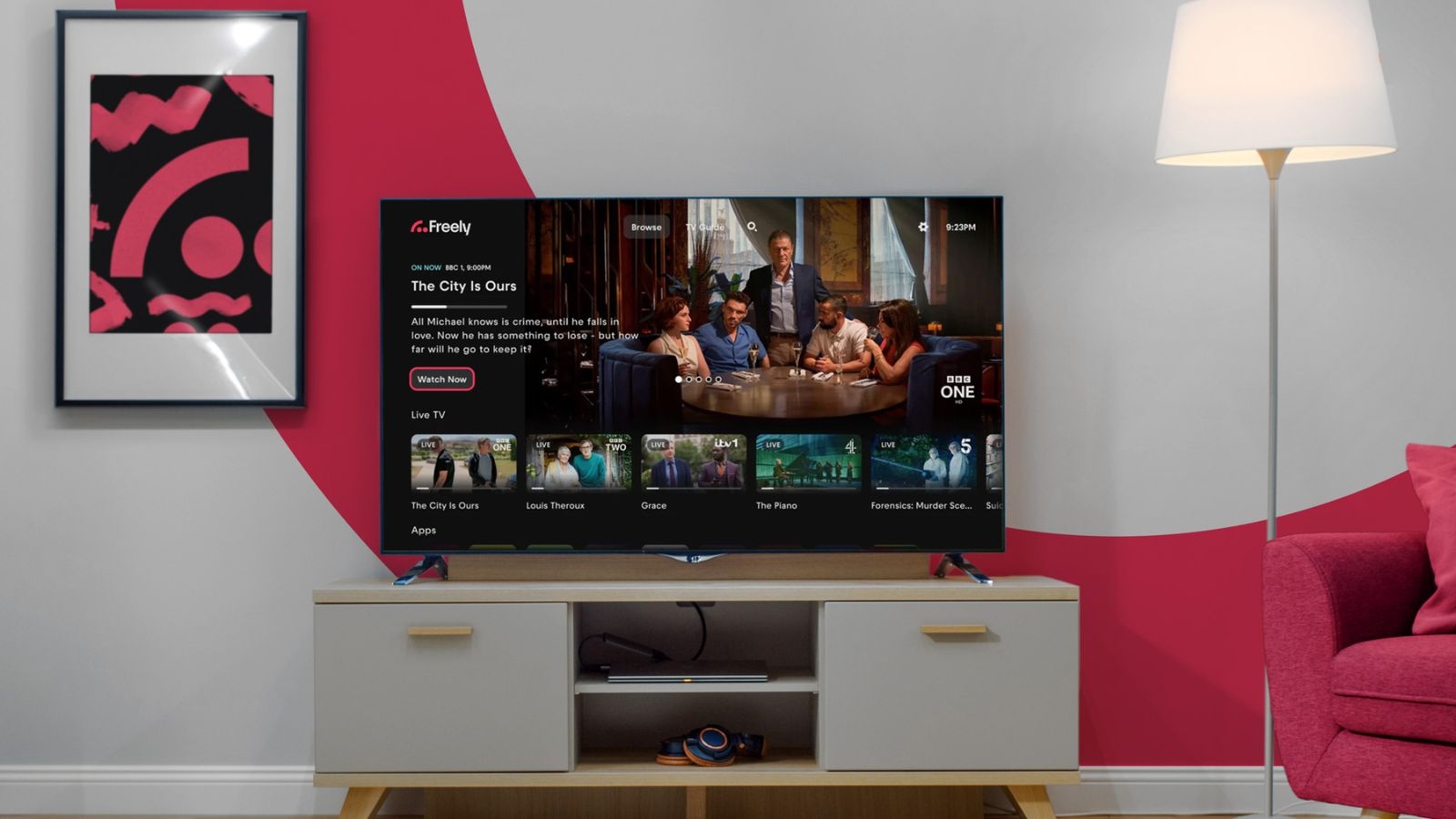 A lounge with a TV on a TV stand with a lamp next to it and the screen displaying the Freely user interface